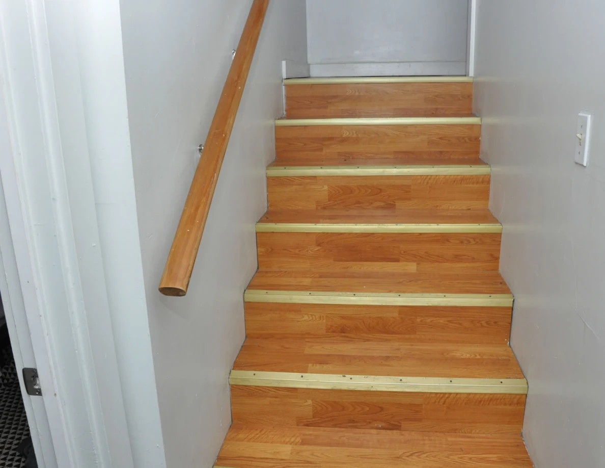 Wooden stairs with pale edge strips and a wooden handrail between white walls.