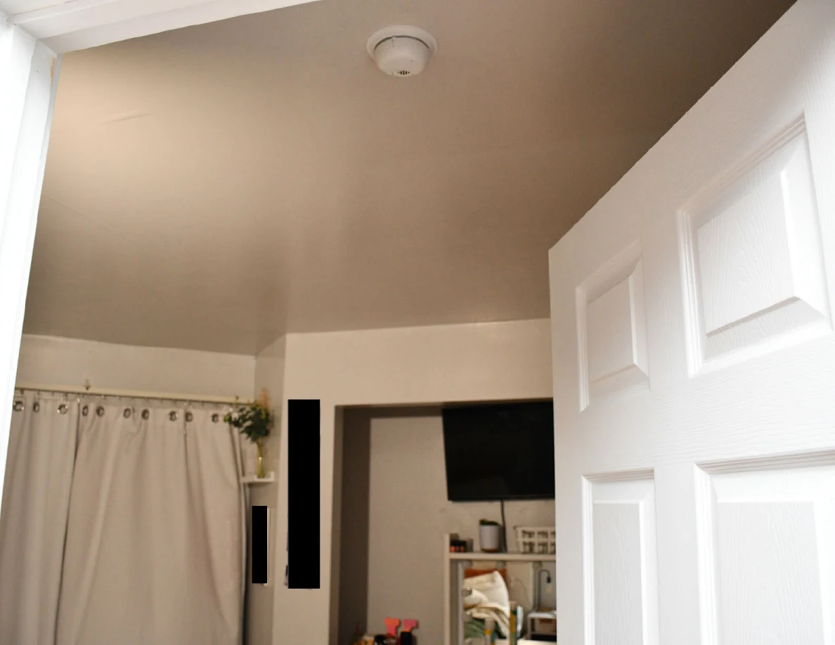 Upper bedroom doorway with a ceiling detector, curtains and television above a vanity.