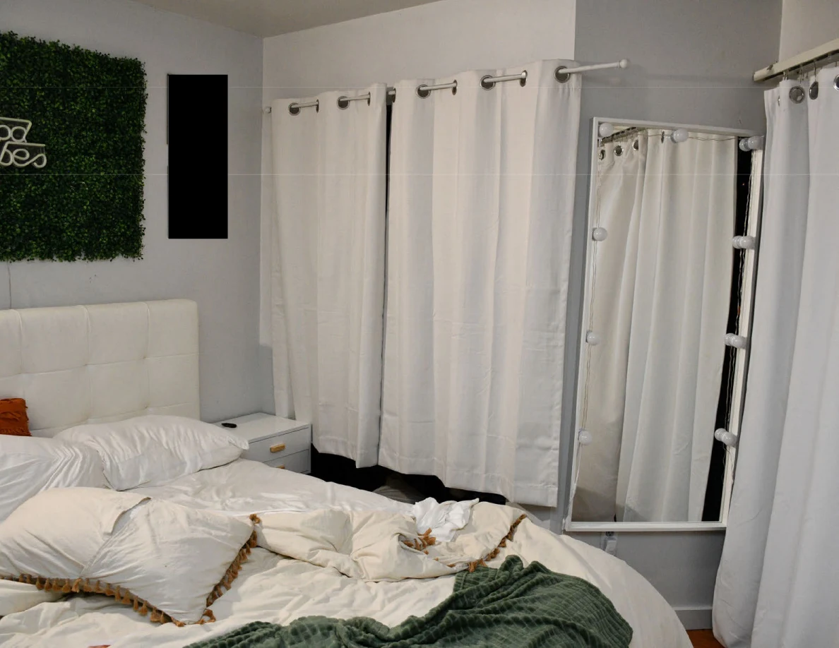 White bed headboard beside curtains and a tall mirror edged with bulbs.