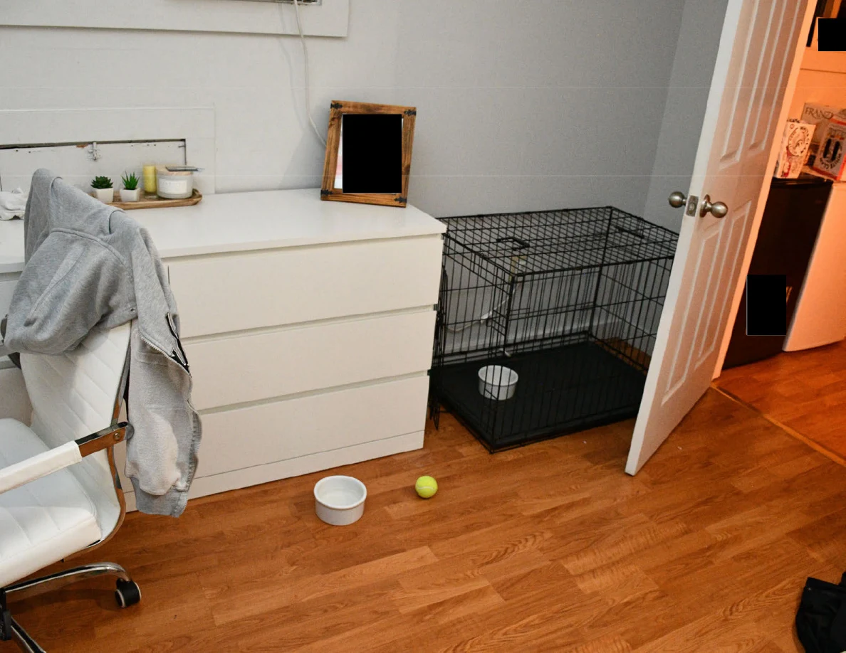 White dresser, rolling desk chair, black wire pet crate, bowl and tennis ball on wooden flooring.