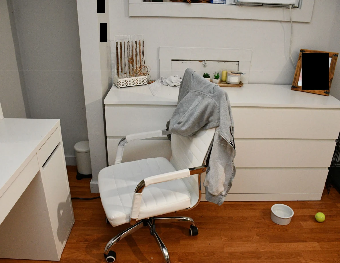 White rolling chair draped with a gray garment in front of a dresser holding jewelry and small plants.