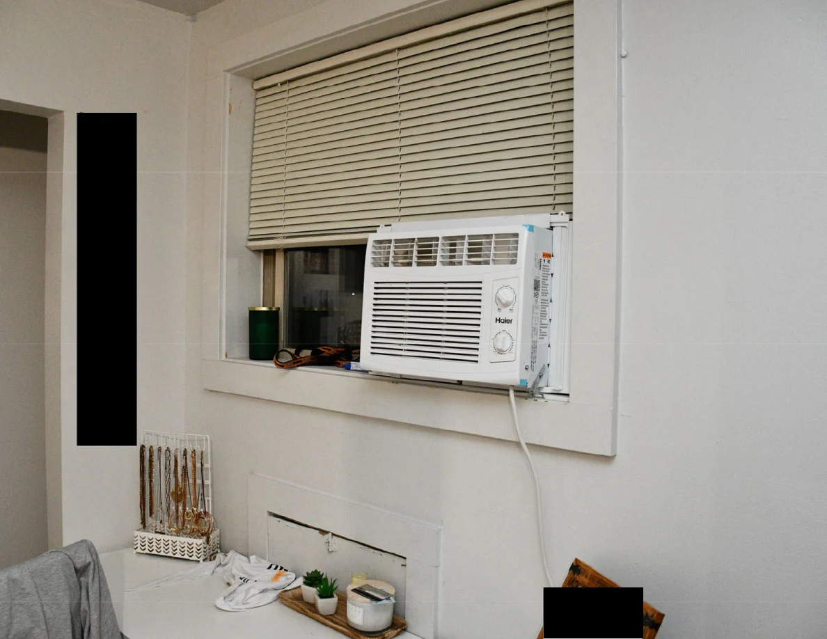 Window air conditioner beneath blinds above a dresser and jewelry organizer.