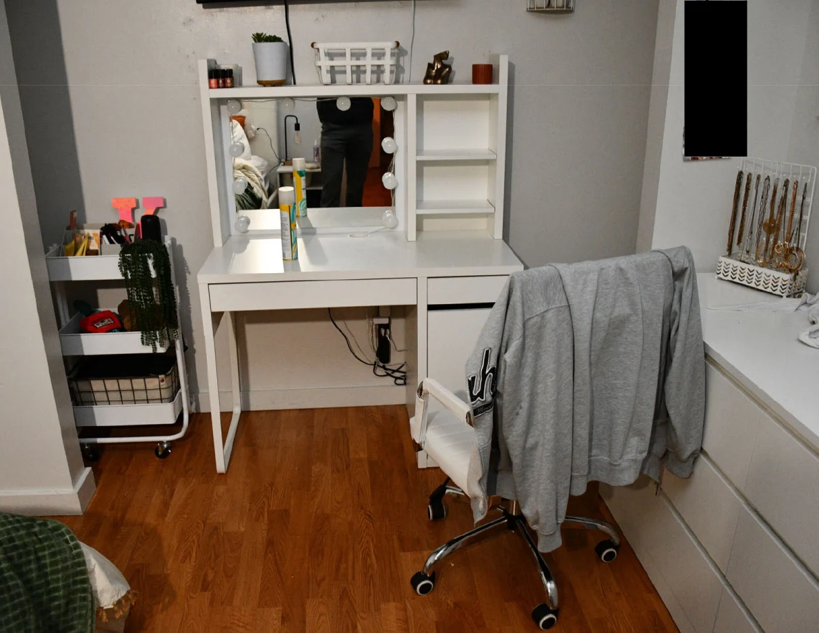 White vanity with mirror and shelves beside a rolling supply cart and garment-draped chair.