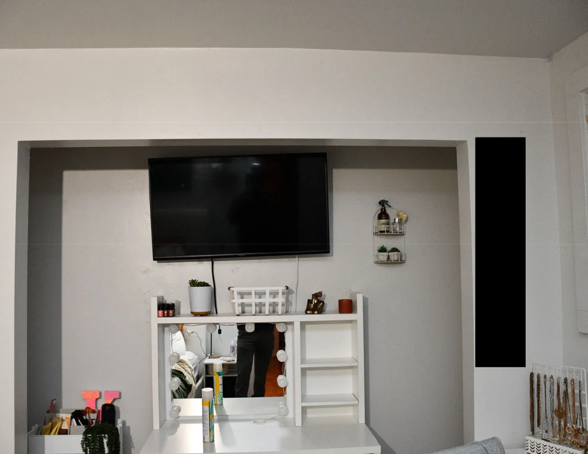 Wall-mounted television above a white vanity mirror and shelves.