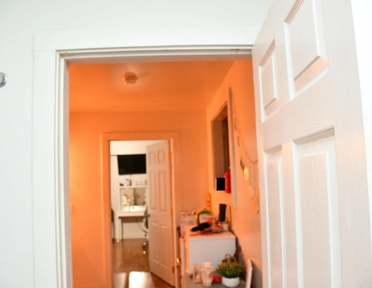 Upper doorway view down an orange-lit hallway toward another room.