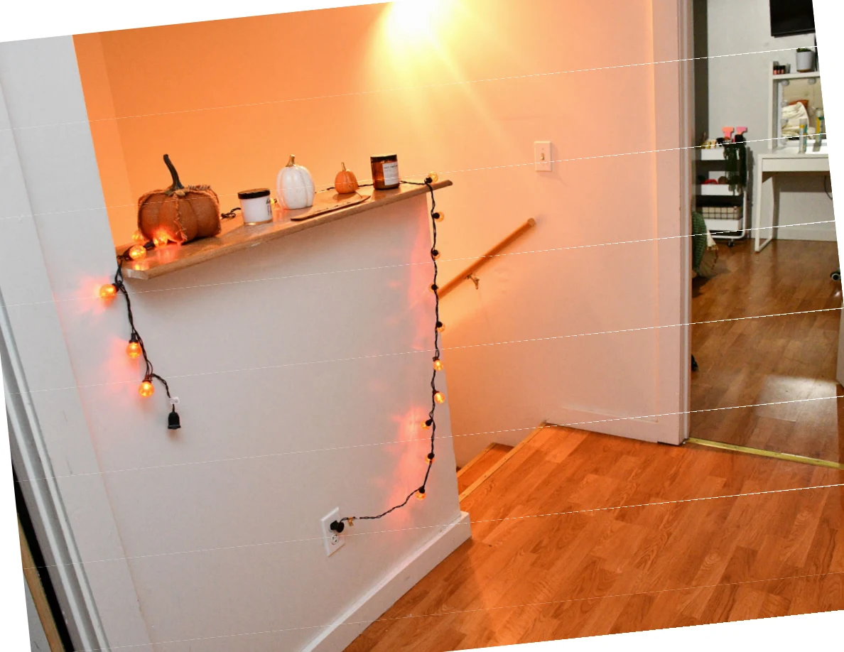 Stairwell landing with a narrow shelf, pumpkin decorations and orange string lights.