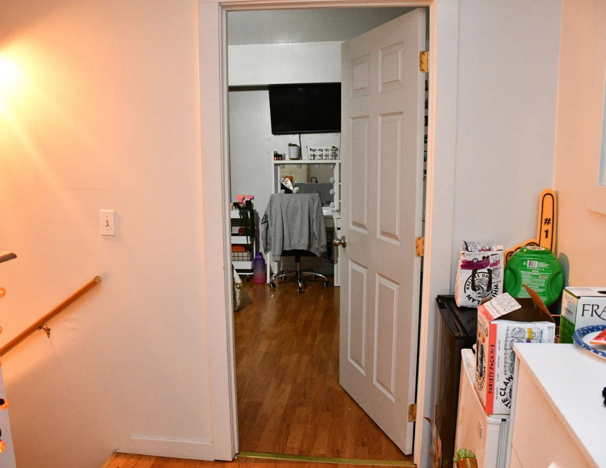 Hallway facing an open bedroom with a vanity and television, with packages and containers at the right.