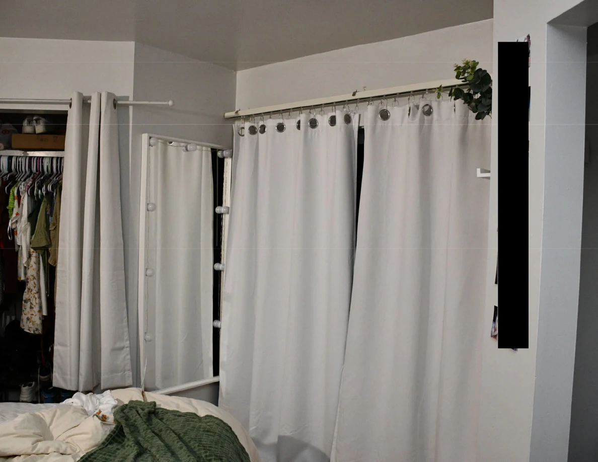 Upper view of white curtains, tall mirror and open closet with hanging clothes.