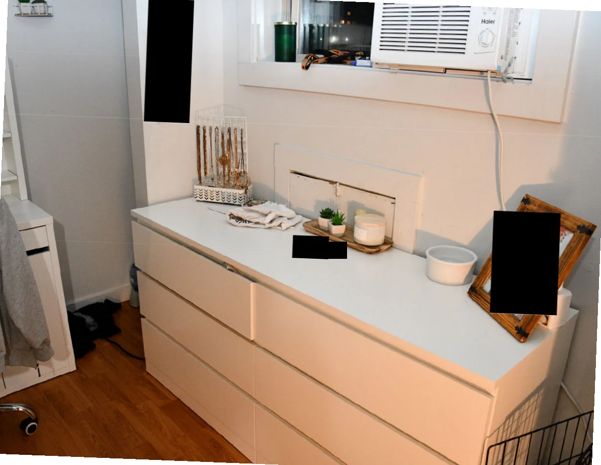 White dresser beneath a window air conditioner, holding jewelry, small plants, bowls and redacted items.