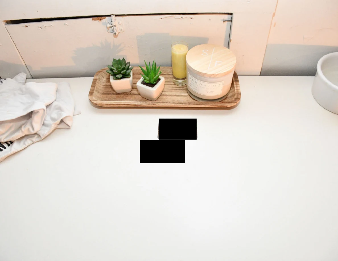 Small potted plants and candles on a wooden tray on a white dresser, with two redacted items nearby.