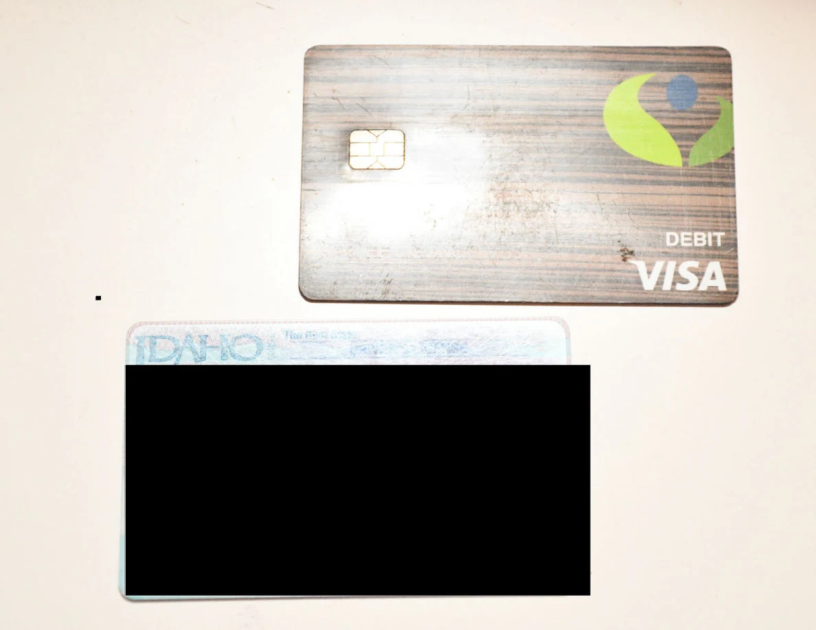 A bank card and partly redacted Idaho identification card on a white surface.