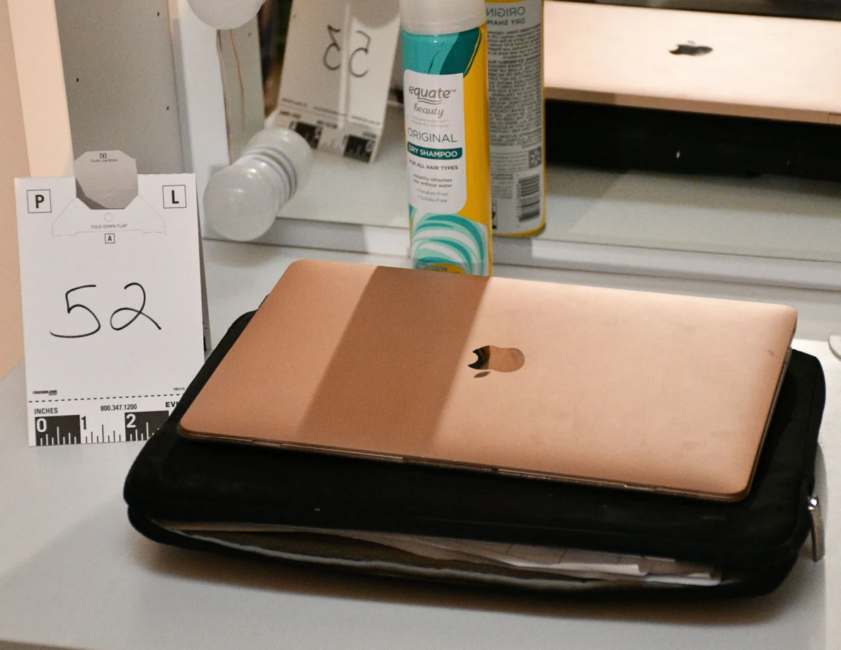 Closed rose-gold laptop on a black case beside scale card 52 at a vanity.