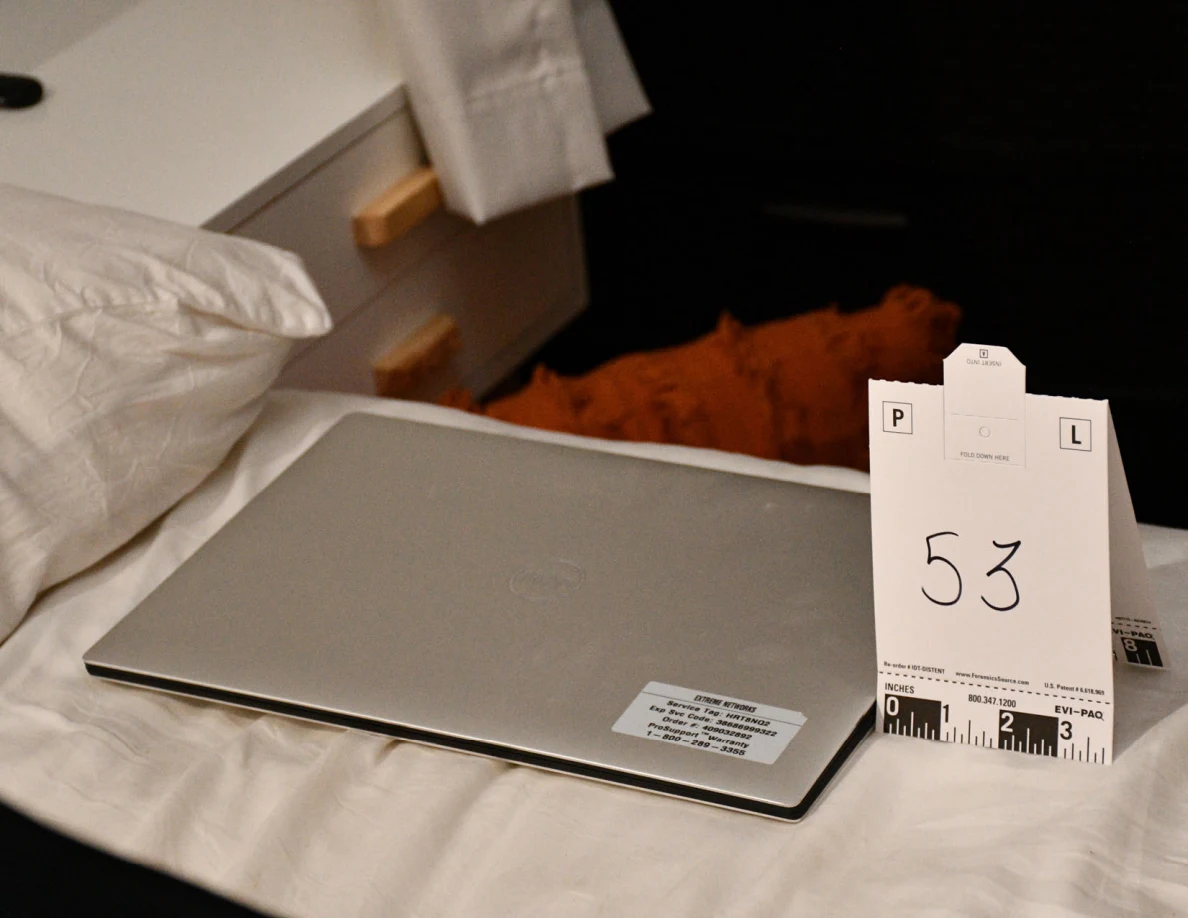 Closed silver laptop on bedding beside scale card 53.