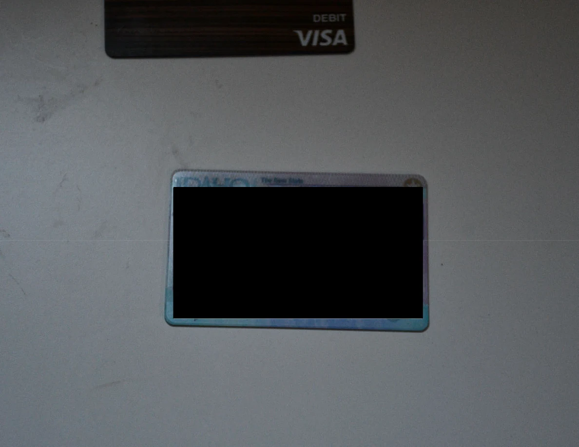 Redacted identification card on a white surface below the edge of a bank card.