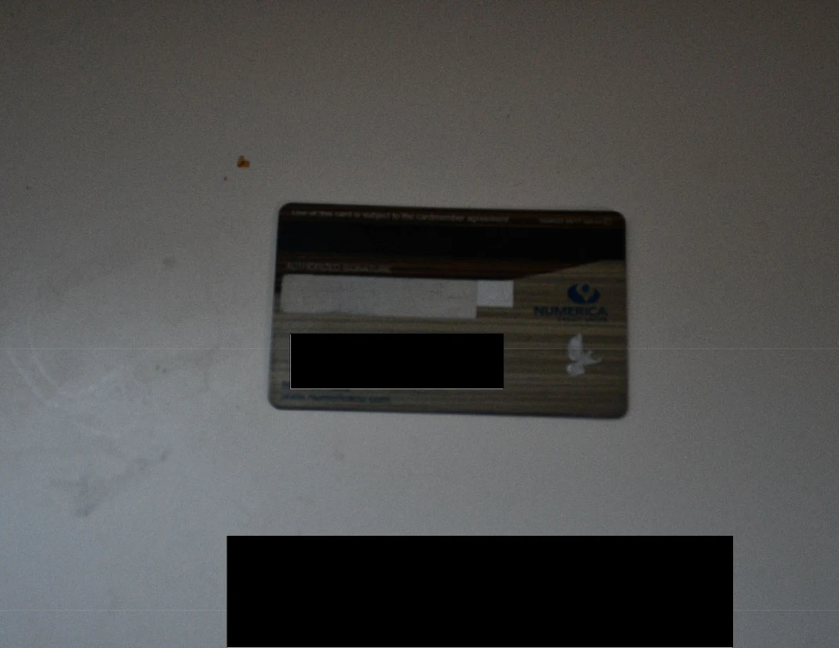 Reverse side of a bank card with a black redaction on a white surface.