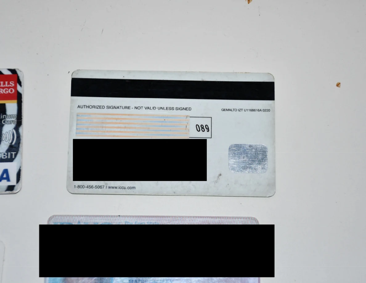Reverse side of a payment card with black redaction, beside other partly visible cards.