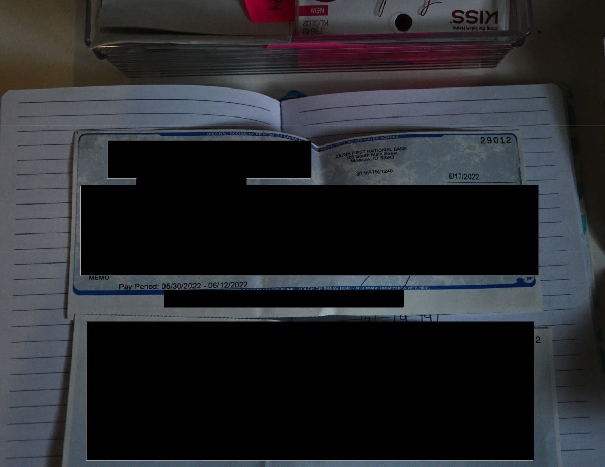 Open lined notebook containing a heavily redacted printed payment document beside cosmetic packaging.