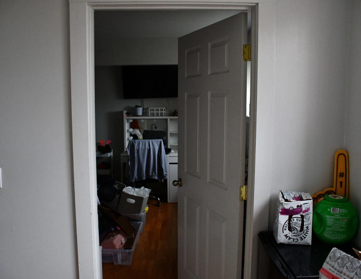 Open bedroom doorway toward a vanity and television, with stacked containers and packages nearby.
