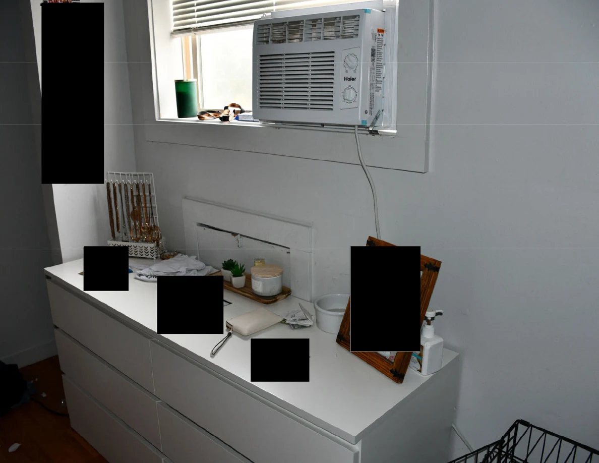 White dresser beneath a window air conditioner, with small plants, jewelry and redacted items.