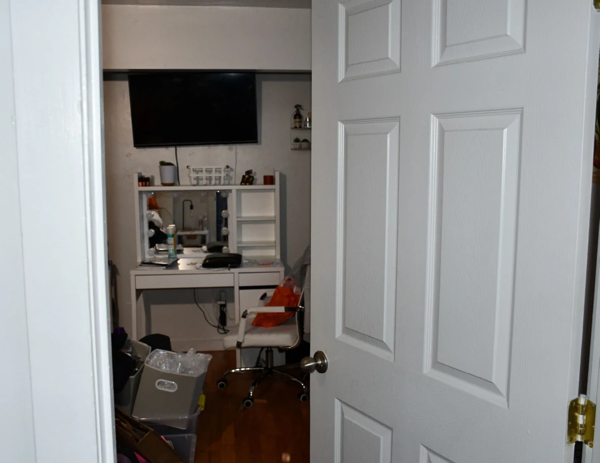 Open white door facing a bedroom vanity and wall television with storage containers below.