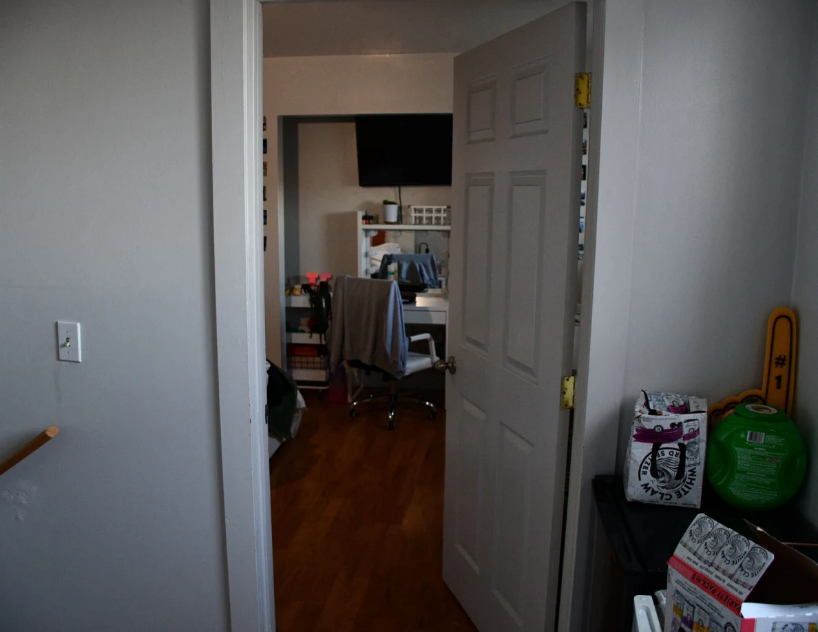 Open bedroom doorway toward a vanity and television, with containers along the hall wall.