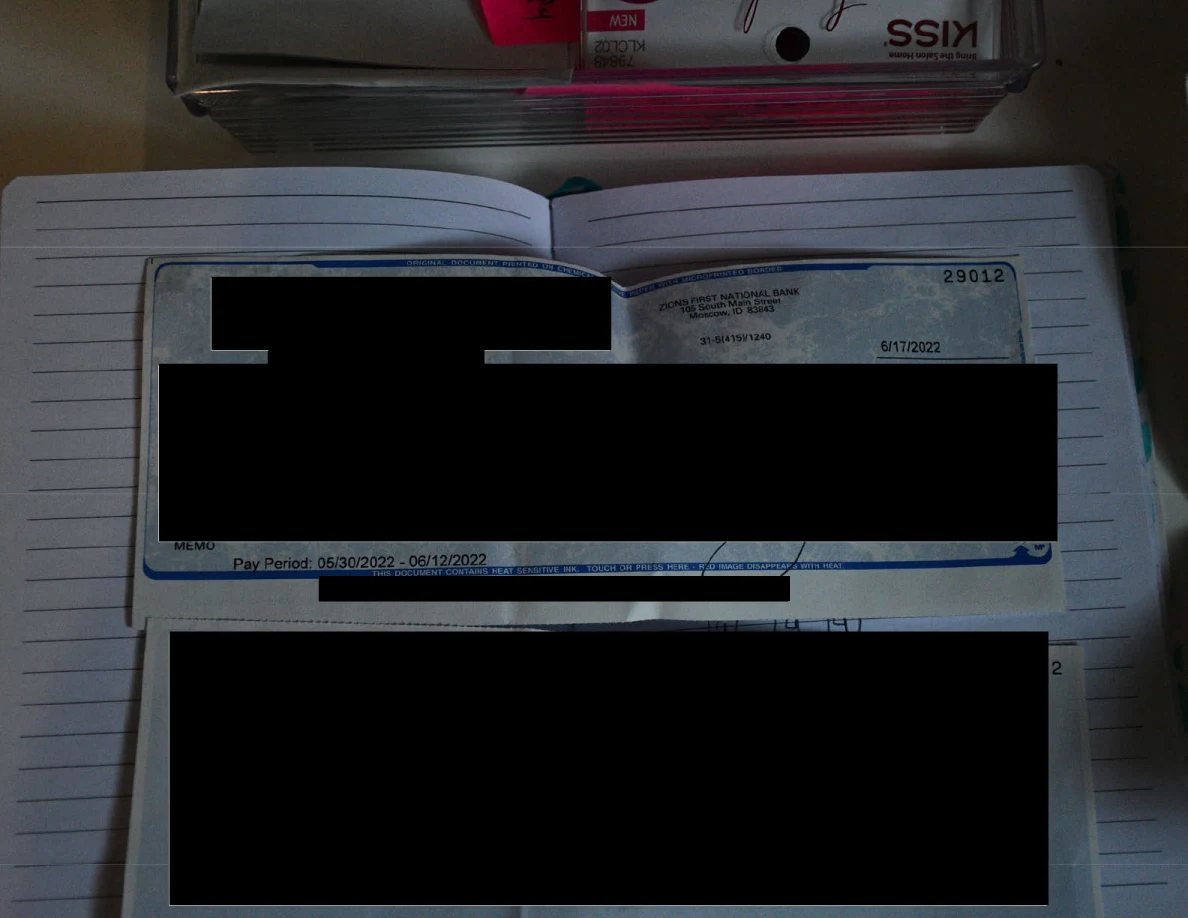 Redacted printed payment document placed across an open lined notebook.