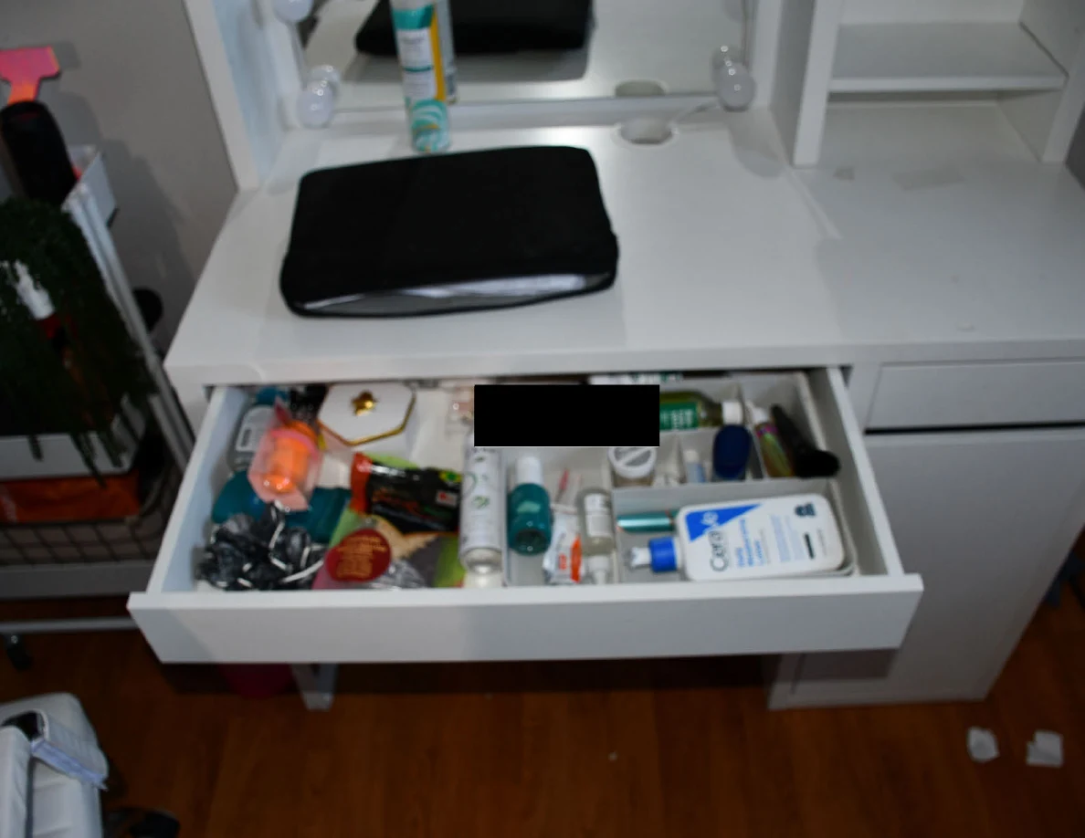 Open wide vanity drawer filled with toiletries and small containers beneath a black case.