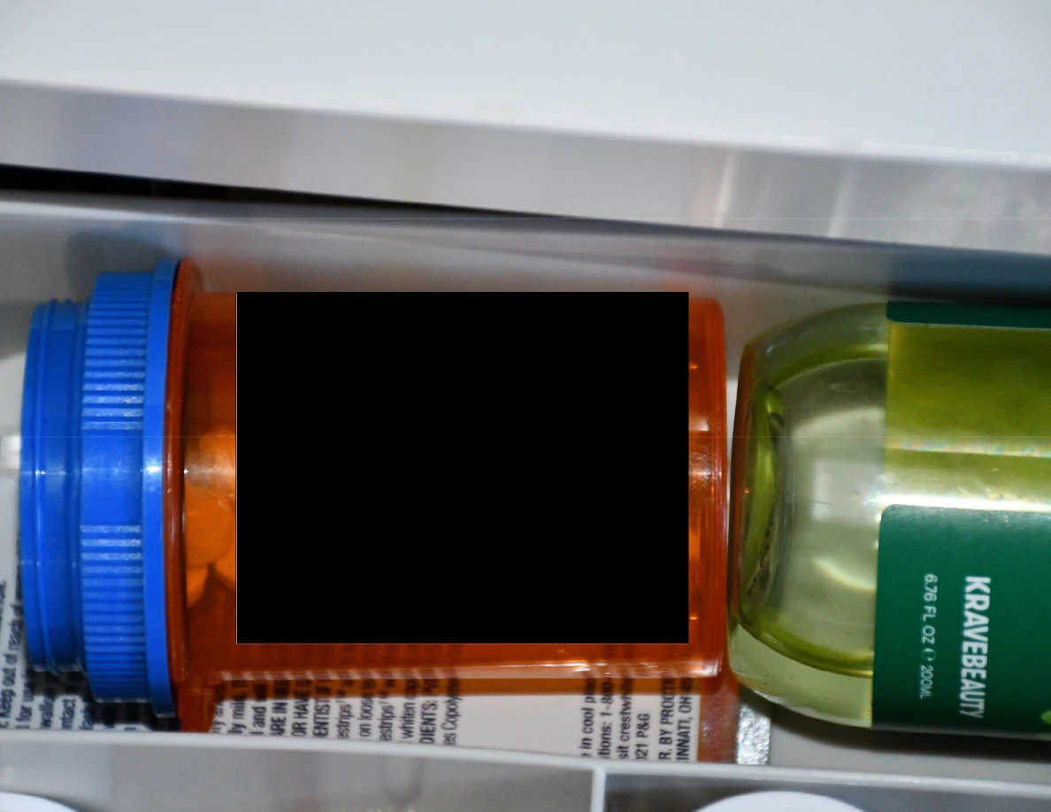 Orange prescription container with a redacted label beside a green toiletry bottle in a drawer.
