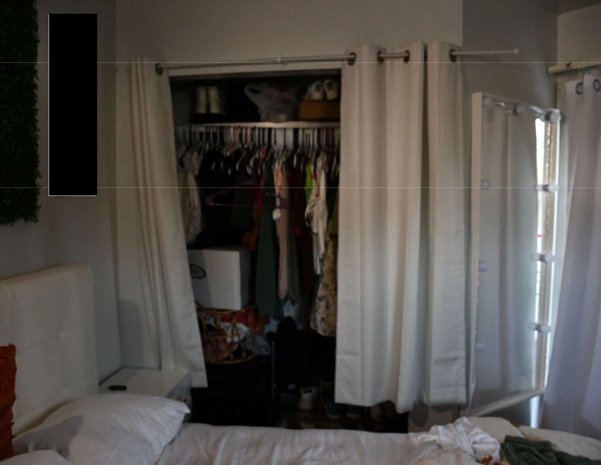 Open clothes closet with hanging garments and shoes beside curtains and a tall mirror.