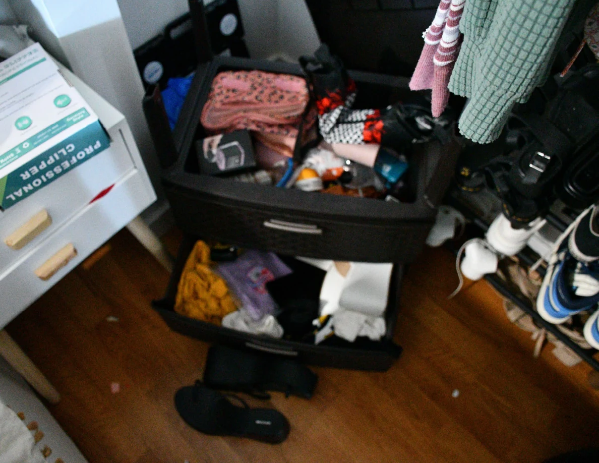Open black drawers containing pouches and small items beside hanging garments and a shoe rack.