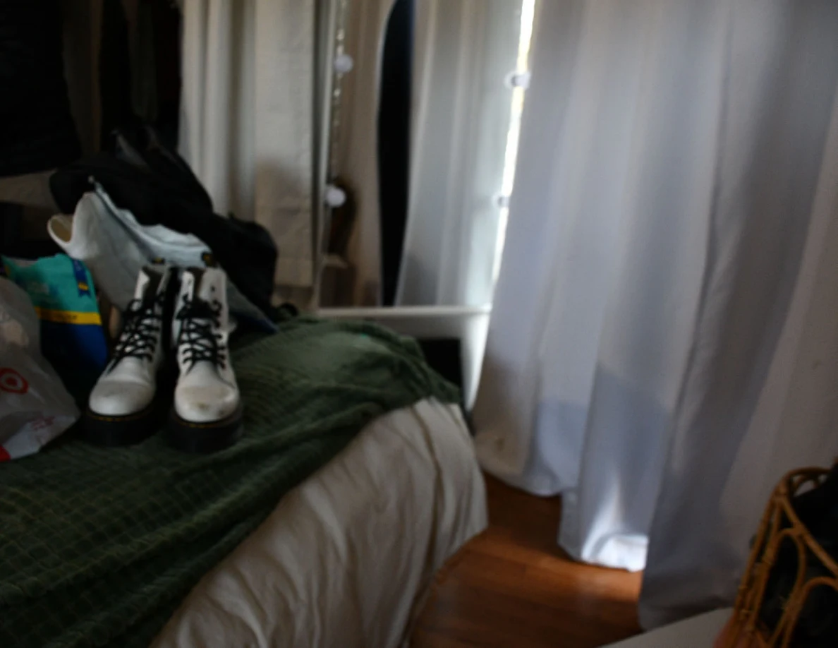 White lace-up boots standing on a green bed blanket beside a mirror and curtain.