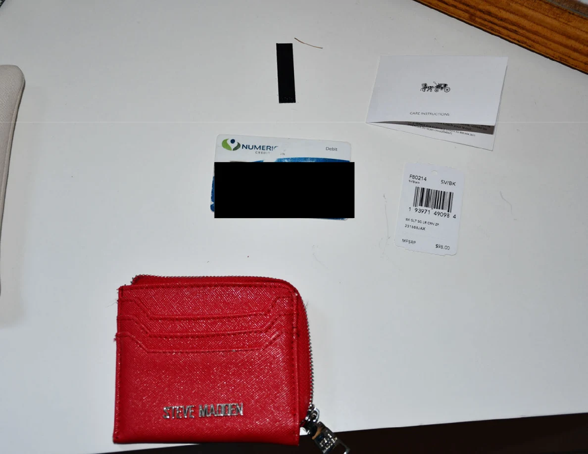 Red card wallet, partly redacted bank card and small paper slips laid out on a white dresser.