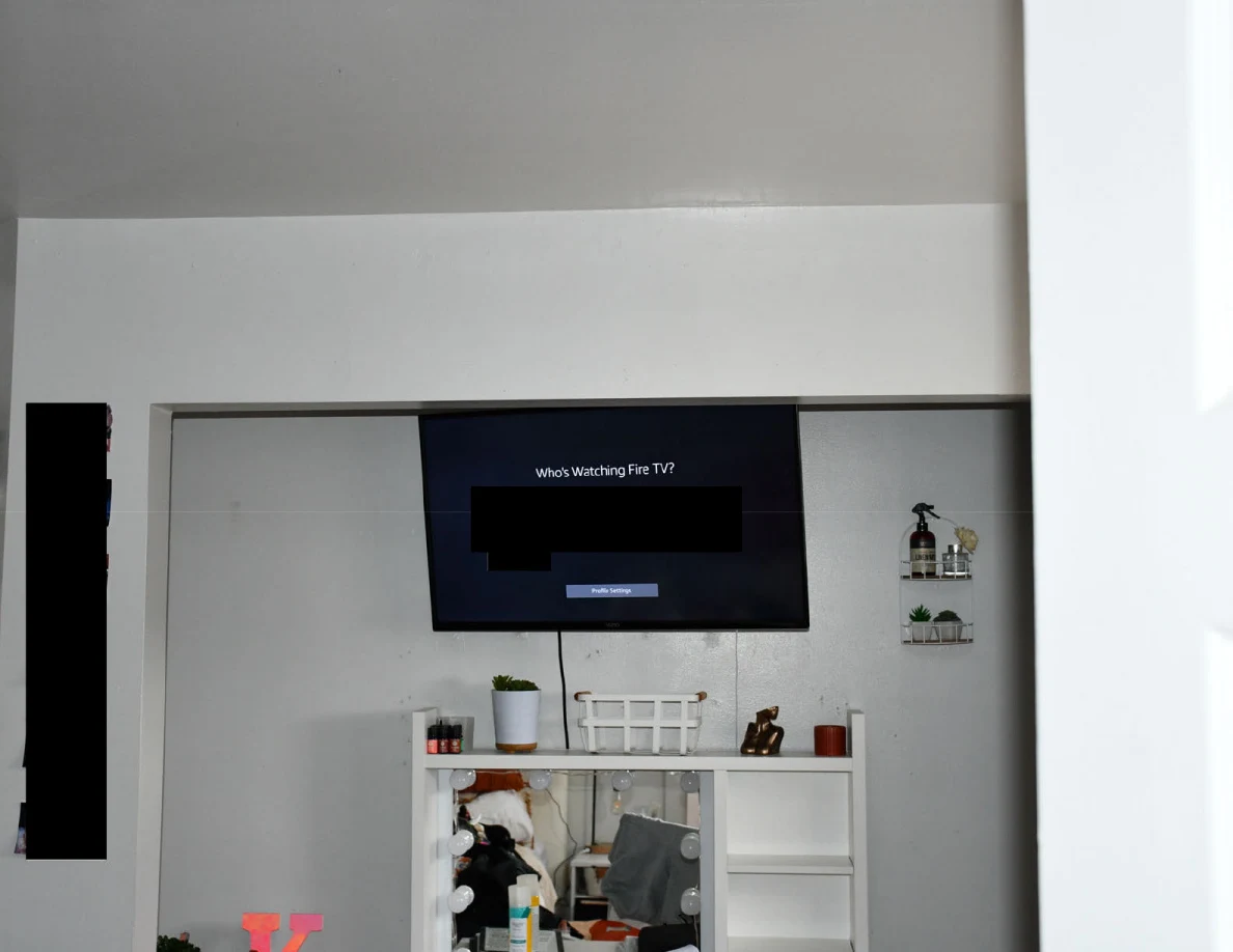 Wall-mounted television showing a streaming prompt above a vanity, with part of the screen redacted.