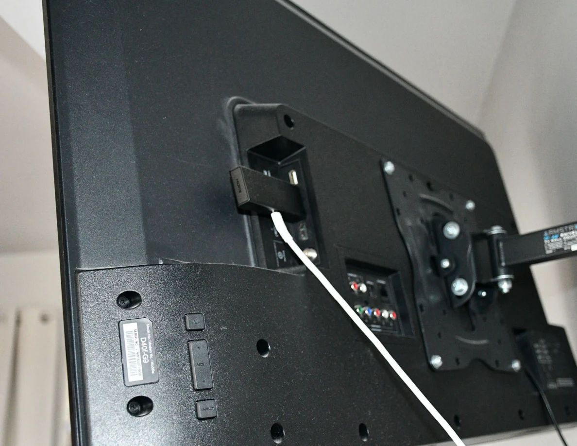 Rear of a television with input ports, wall mount and attached small black device and cable.