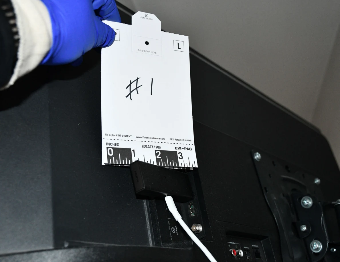 Blue-gloved hand holding scale card 1 beside a small black device connected to a television.