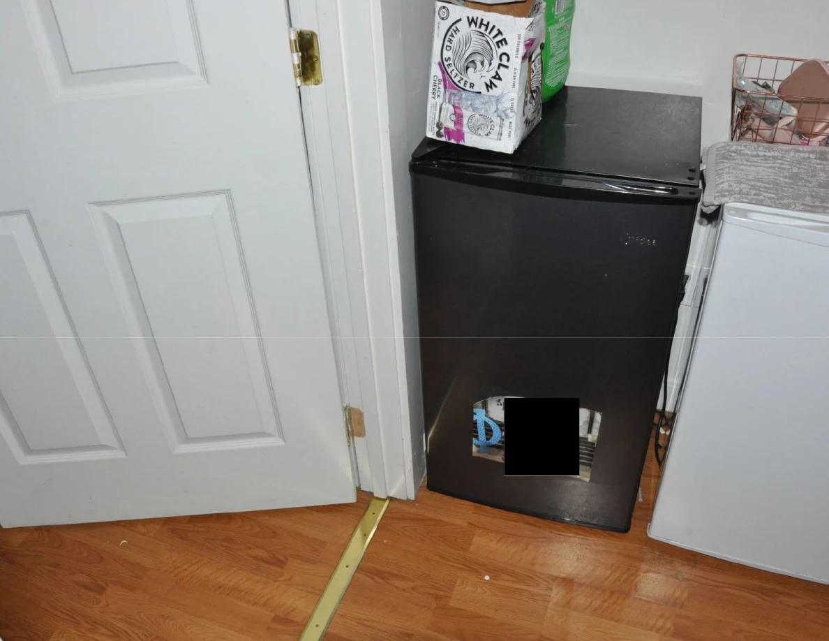 Black mini refrigerator beside a white appliance and paneled door, with drink packaging on top.