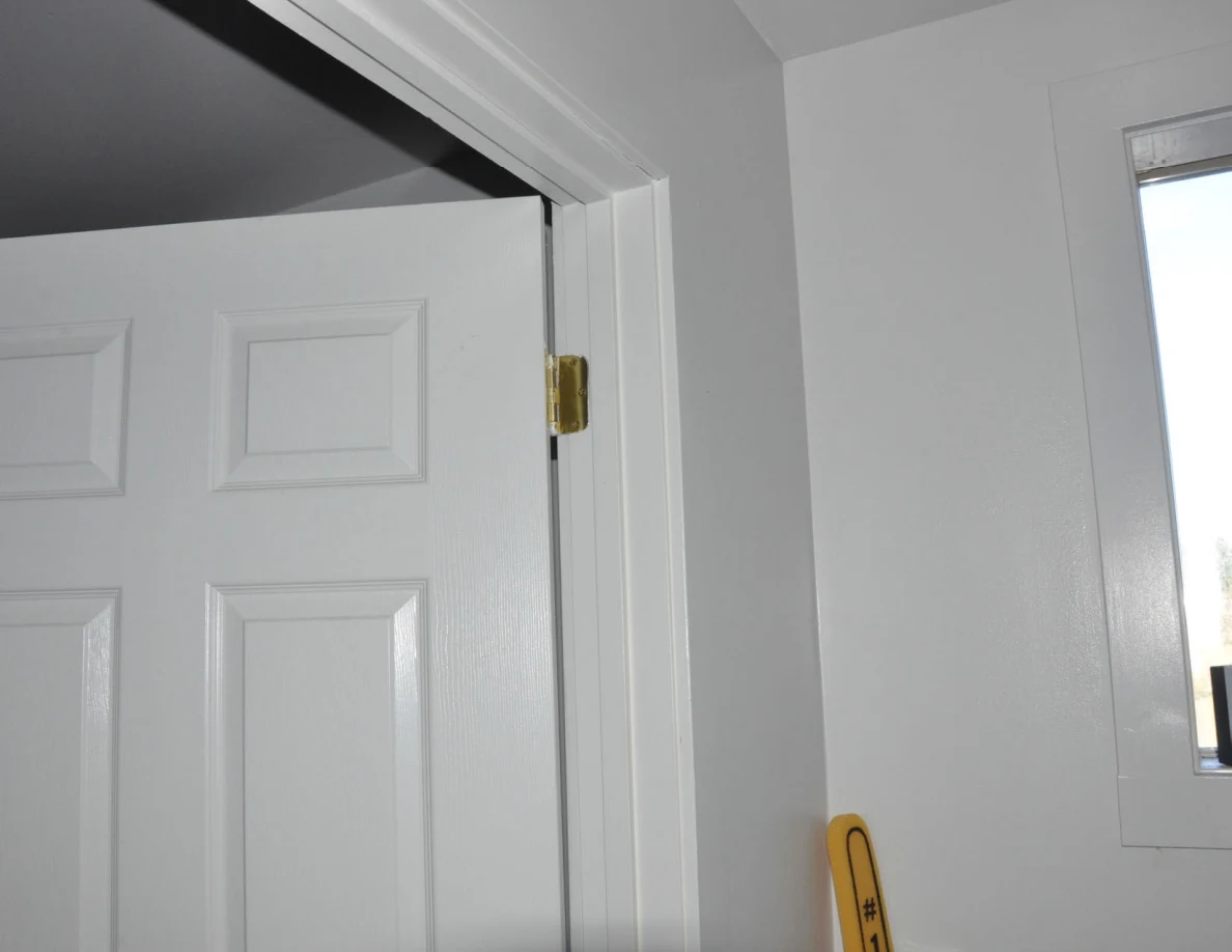 Upper edge and hinge of an open white paneled door beside a window.