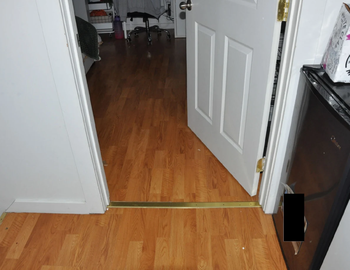 Wood-pattern floor through an open bedroom doorway beside a mini refrigerator.