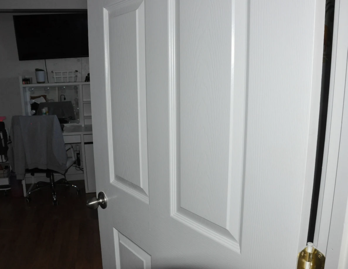 Close angled view of a white paneled door with its knob and hinge.
