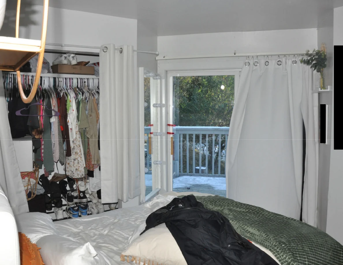 Bed with green blanket and dark clothing facing an open balcony door and clothes closet.