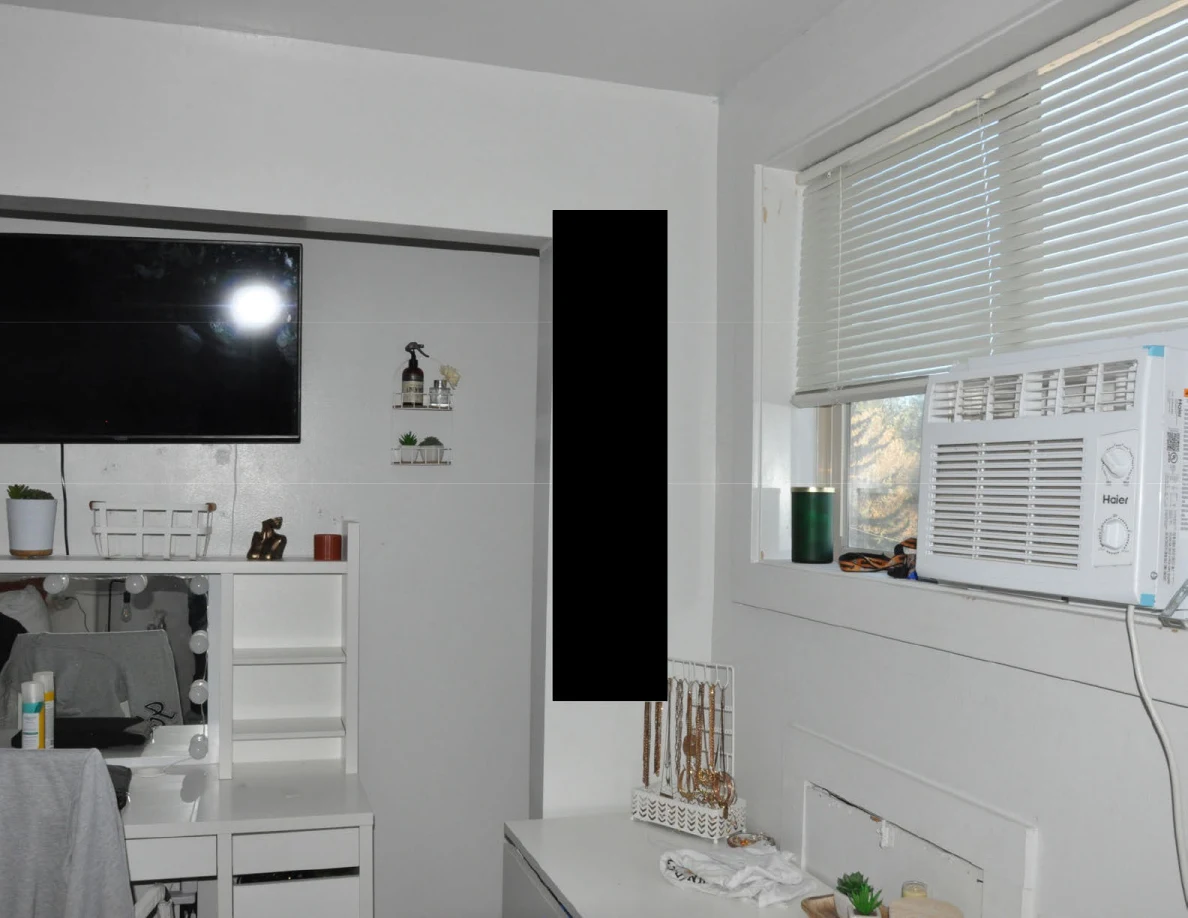 Television and vanity beside a window air conditioner beneath blinds.