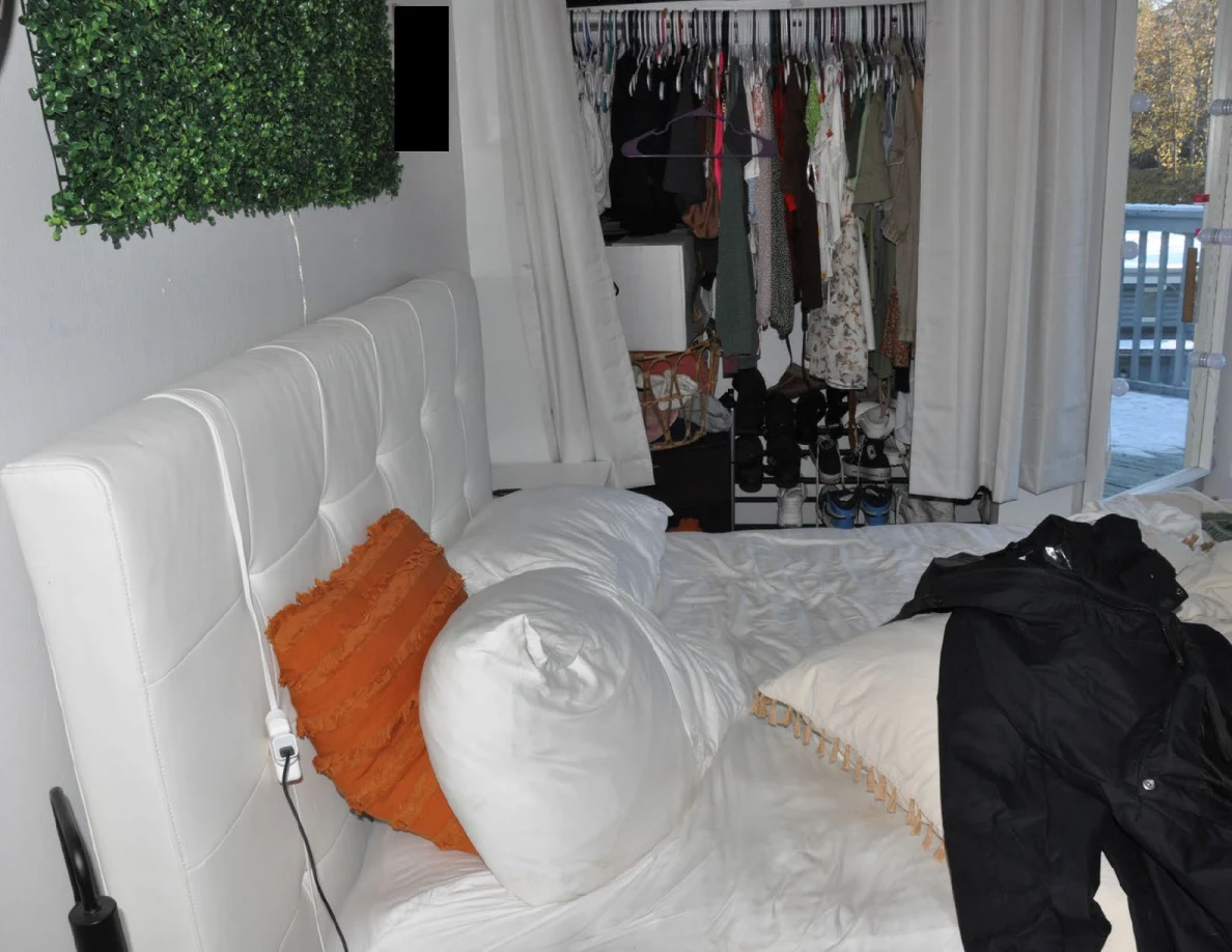 White upholstered bed headboard and pillows with dark clothing on the bed and an open closet beyond.