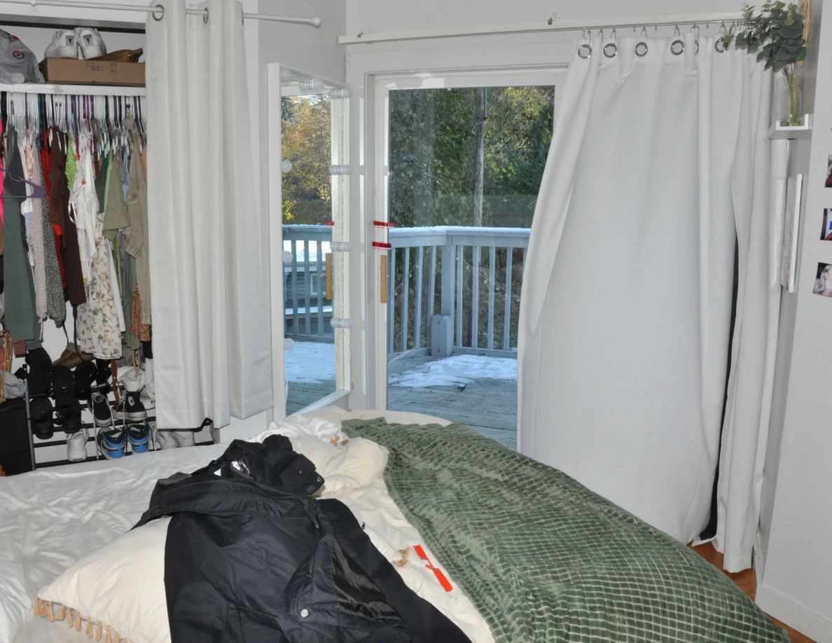 Bed with dark clothing and green blanket beside an open glass balcony door.