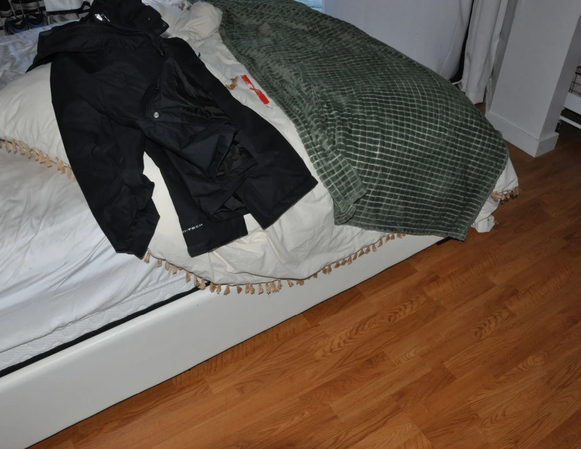 Dark garment spread on a white bed beside a green textured blanket.