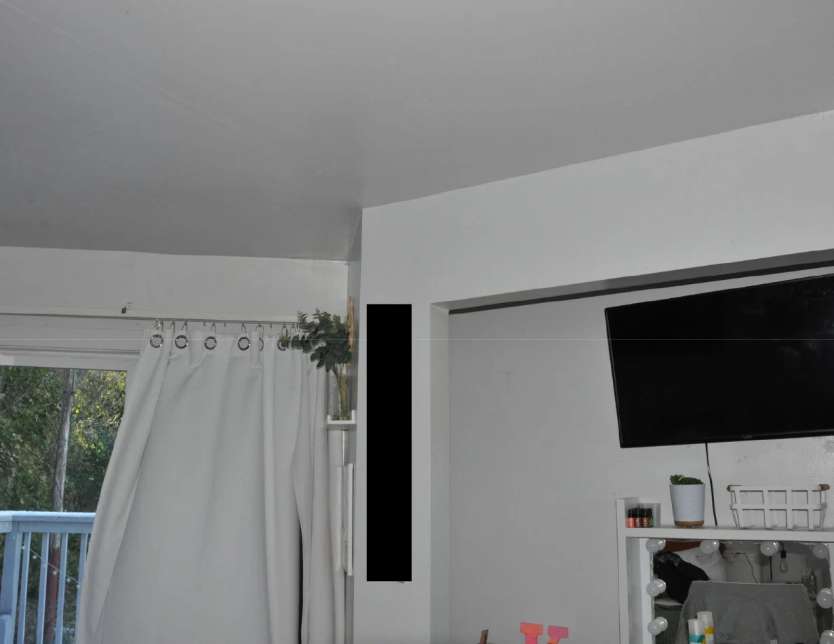 Upper bedroom wall with television and curtain beside a balcony doorway.