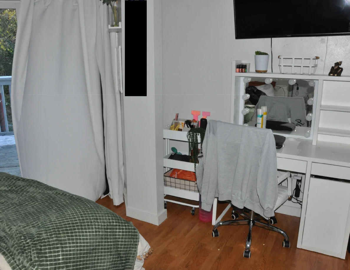 White vanity and rolling chair beside a supply cart and the foot of a bed.
