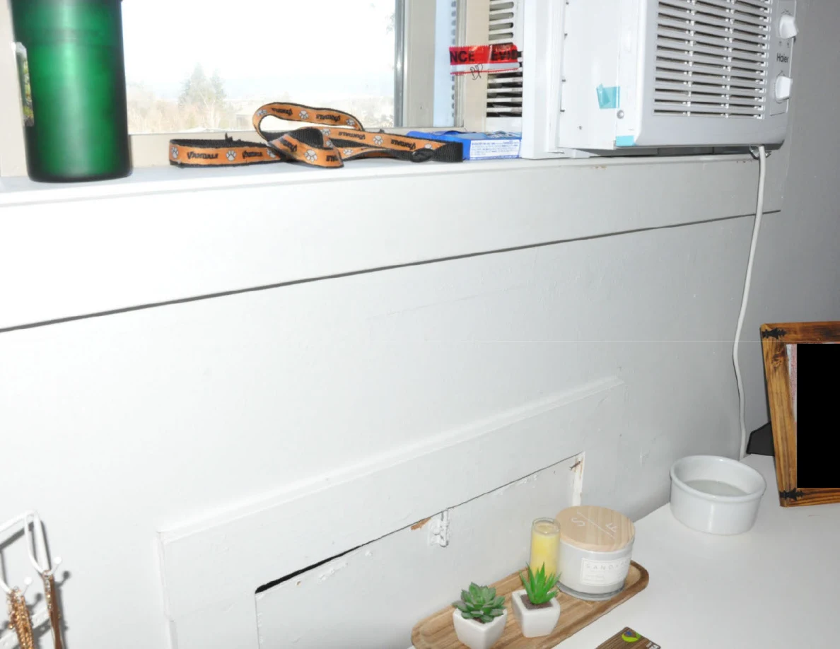 Window sill with green tumbler, strap and air conditioner above a dresser.
