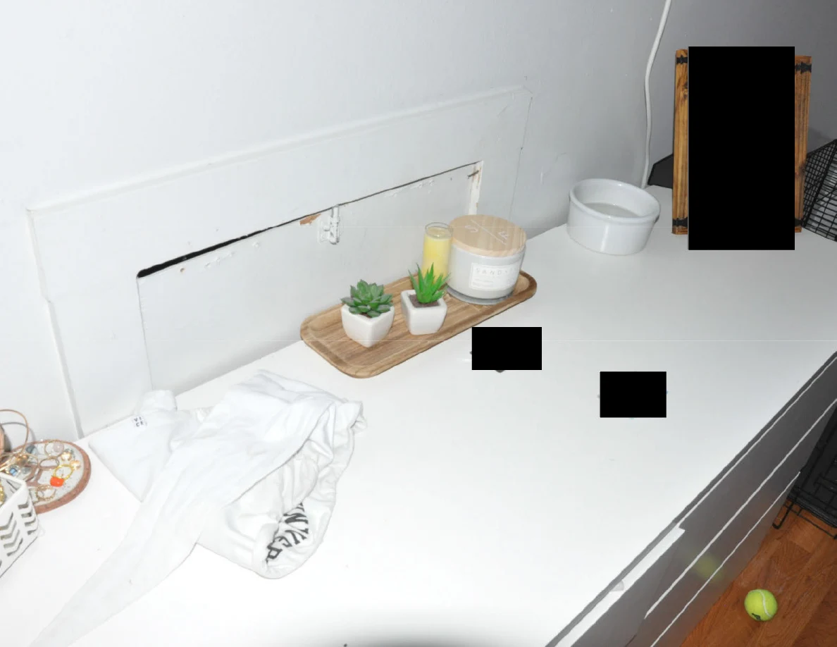 White dresser with folded fabric, small plants and candles on a tray, plus redacted items.