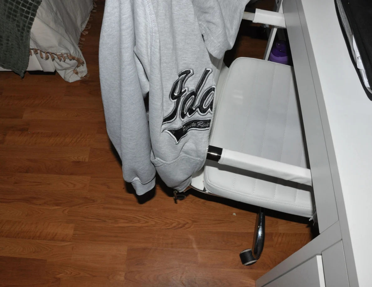 White rolling chair draped with a gray sweatshirt beside a vanity.