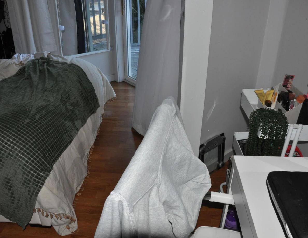 Chair draped in gray fabric between a bed with green blanket and a supply cart.